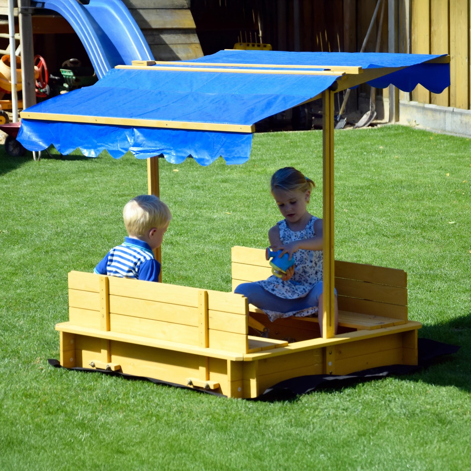 Dobar Sandkasten mit blauem Dach, Kinder spielen im gelben Holzsandkasten mit Sitzbänken.