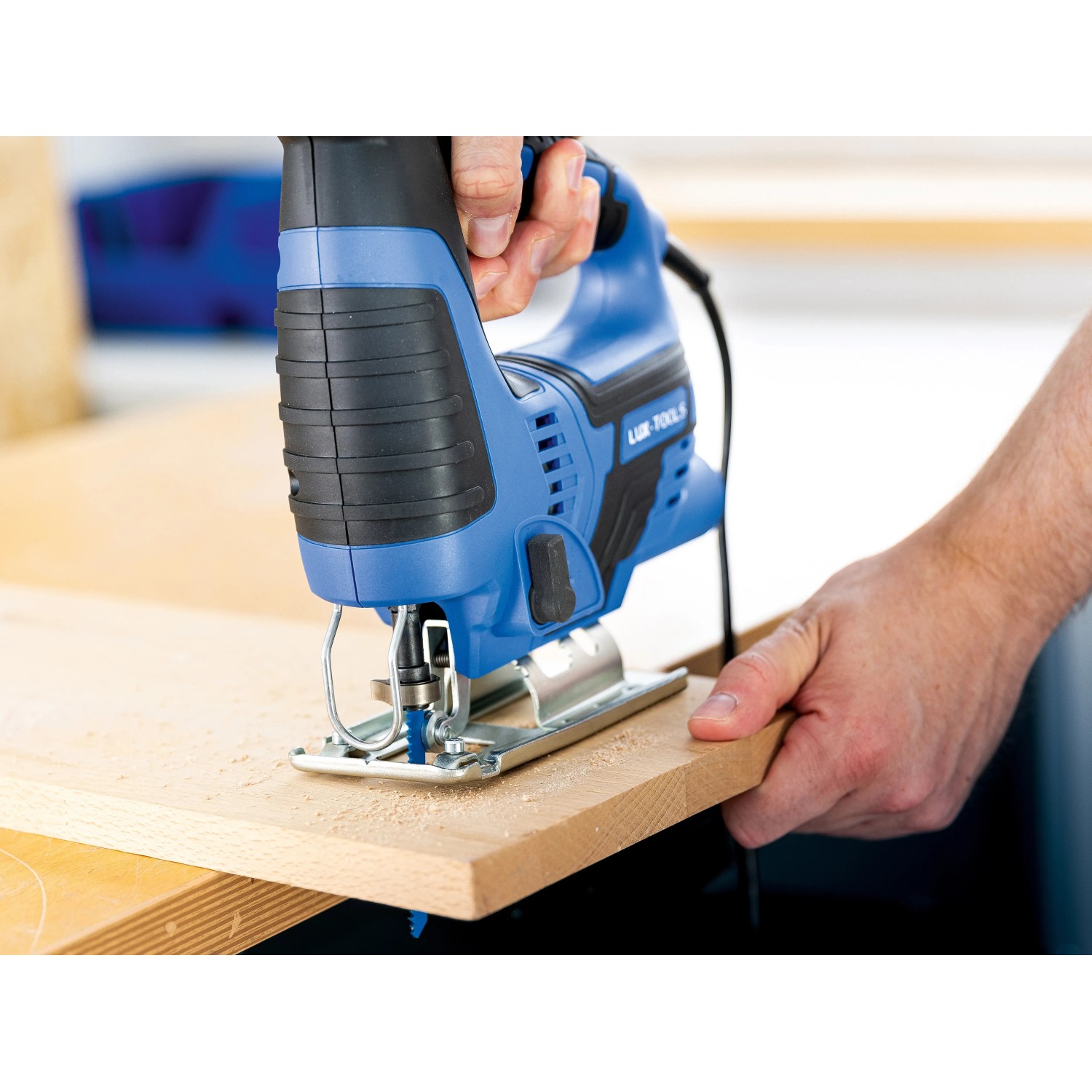 Blaue LUX Stichsäge E-STS-23 schneidet Holzbrett. Handwerkzeug für präzise Schnitte.