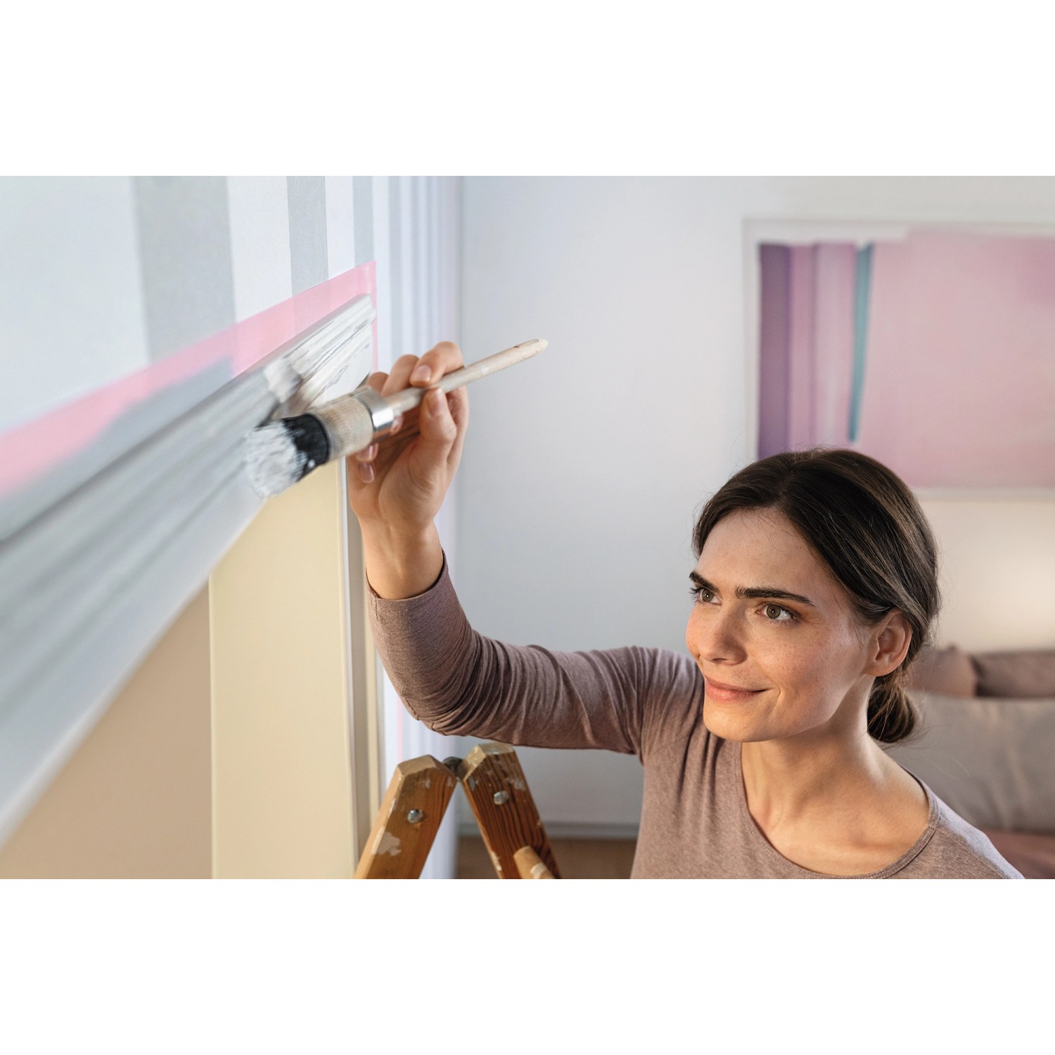 Frau streicht Wand mit Tesa Malerband Professional Sensitive als Schutz.