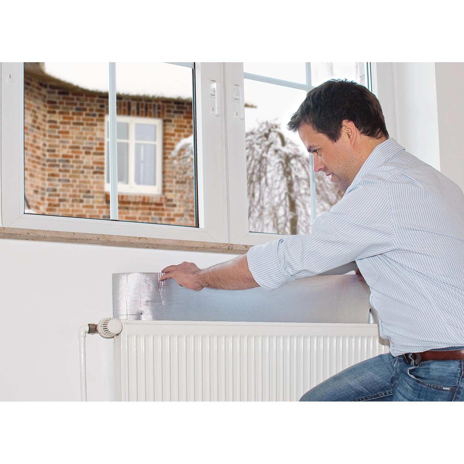 Mann montiert Tesamoll Heat Reflector Reflektierfolie hinter Heizkörper zur Wärmereflektion.