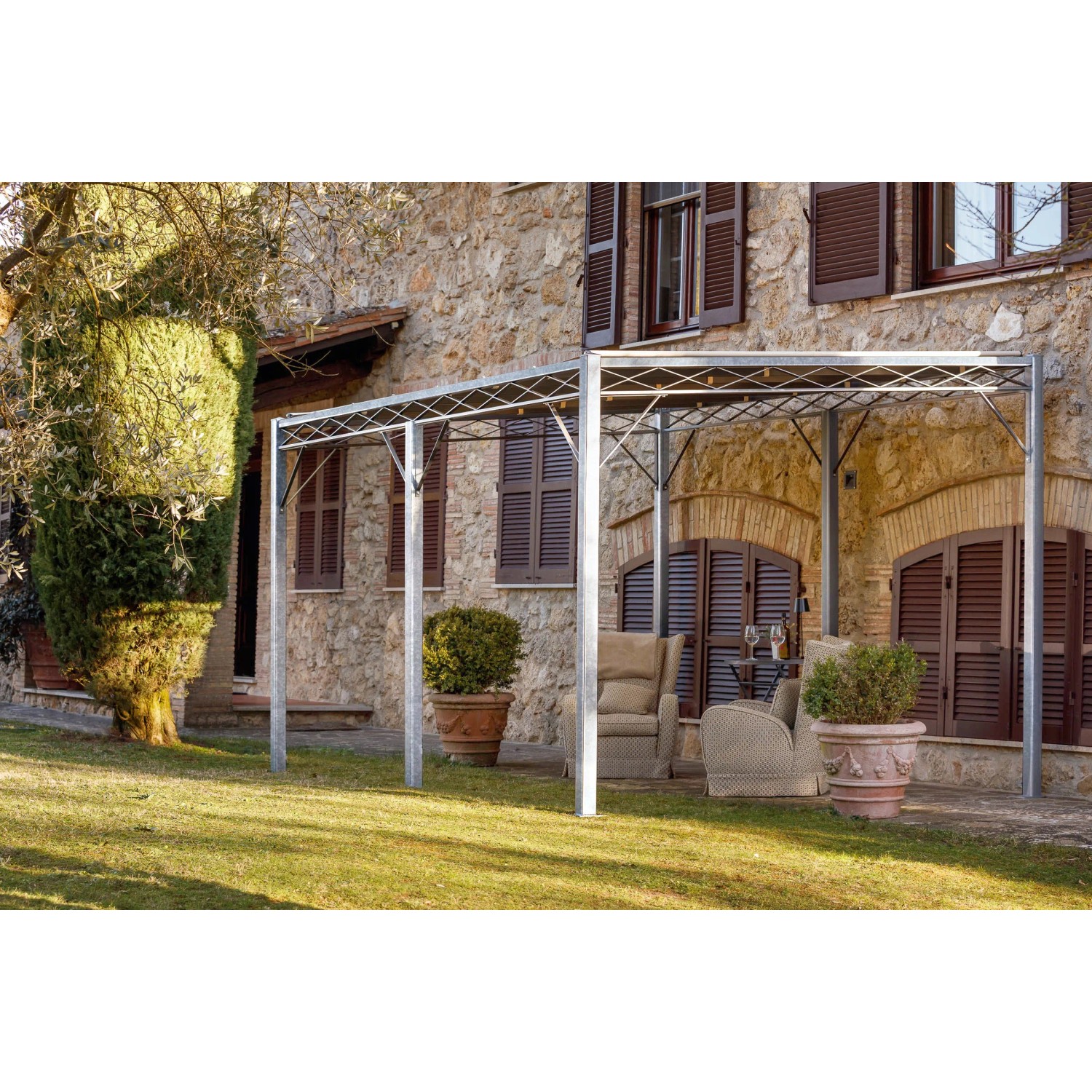 Feuerverzinkte Eleo Pergola Metall Sicilia (252,2x408x304 cm) vor Hauswand mit Gartenmöbeln.