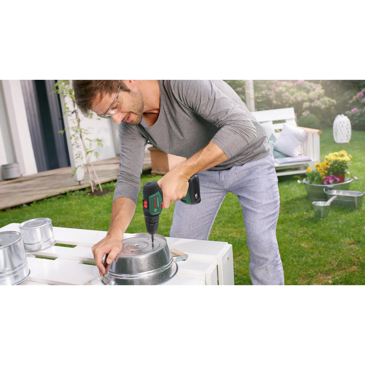 Mann bohrt mit dem Bosch 18V Akku-Bohrschrauber UniversalDrill 18V Solo ein Loch in einen Metalleimer.