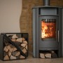 Schwarzes Westmann Kaminholzregal (57x36x56cm) neben Kaminofen mit Holzscheiten.