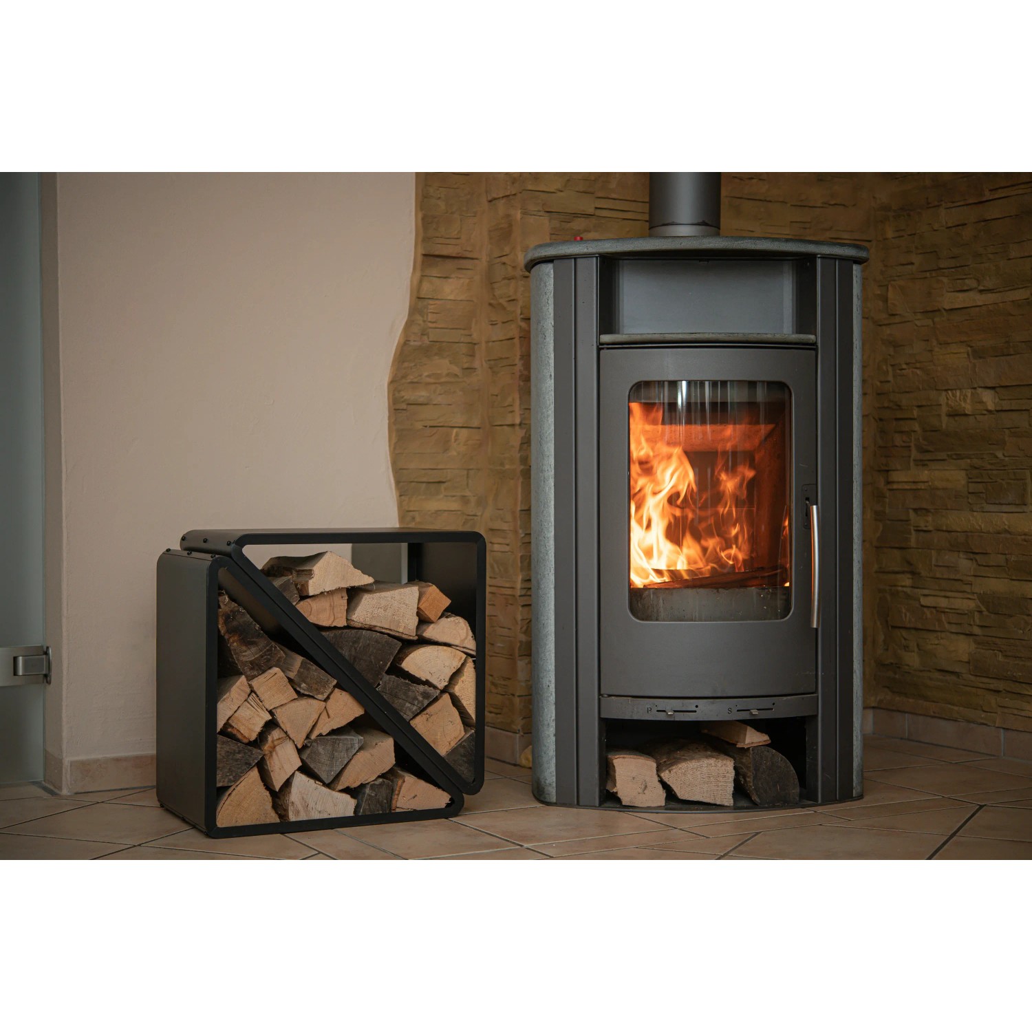 Schwarzes Westmann Kaminholzregal (57x36x56cm) neben Kaminofen mit Holzscheiten.