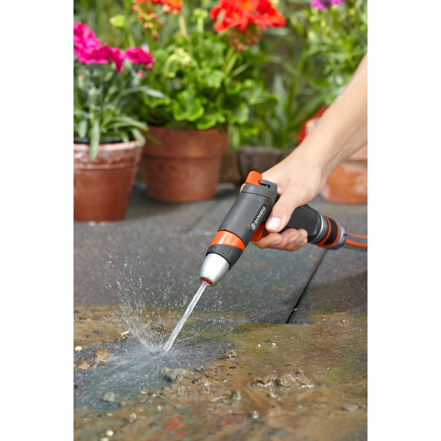 Gardena Premium Reinigungsspritze in Aktion: Wasserstrahl reinigt Steinboden im Garten.