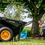 Schwarze Polar Schubkarre Cub Cart mit gelben Rädern und Frau bei Gartenarbeit.