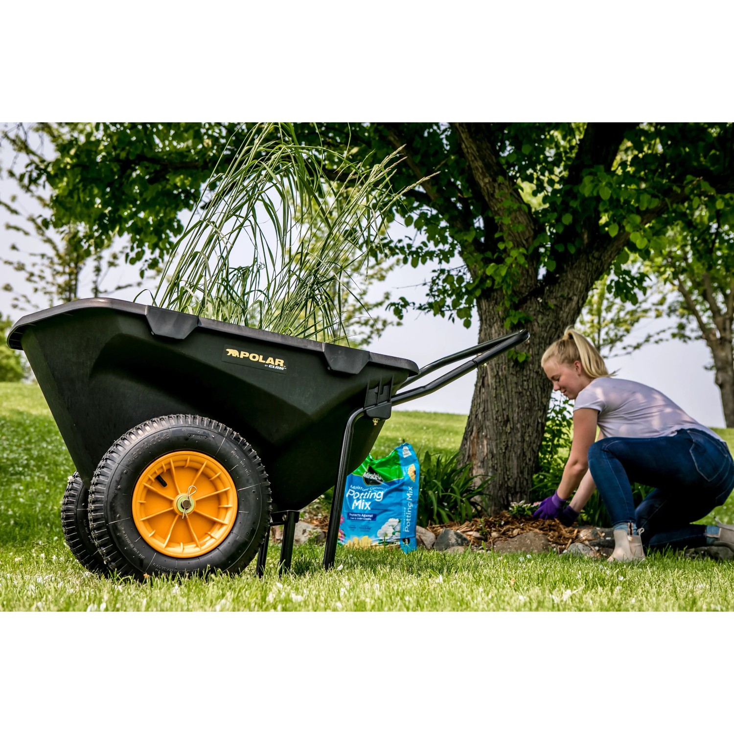 Schwarze Polar Schubkarre Cub Cart mit gelben Rädern und Frau bei Gartenarbeit.