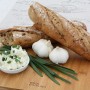 Brot, Knoblauch und Kräuterquark auf Holzbrett. Garten-Knofi als Zutat.