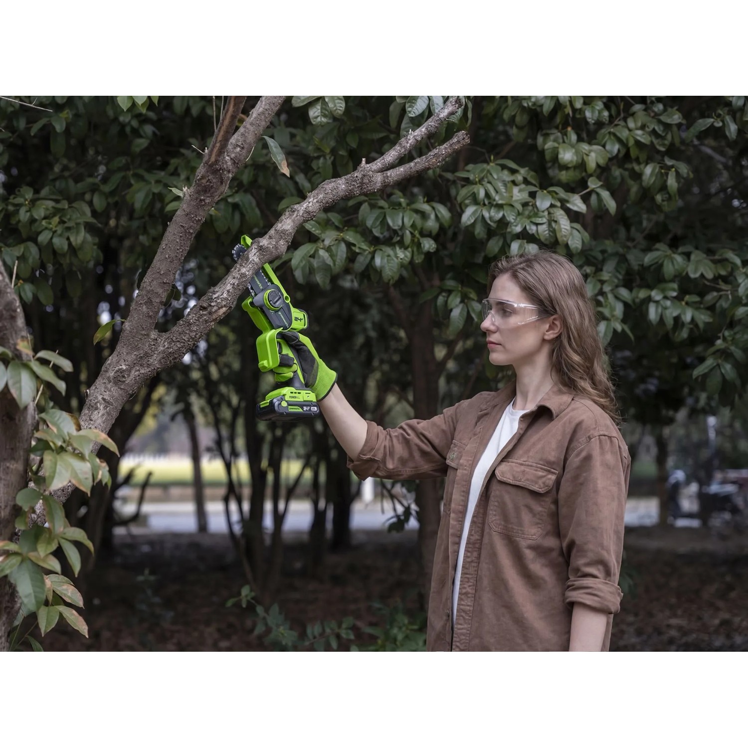 Frau schneidet Ast mit Greenworks Akku-Kettensäge (Schwert 10 cm).