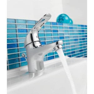 Glänzende Grohe QuickFix Waschtischarmatur Swift Chrom mit Wasserstrahl vor blauem Mosaik.
