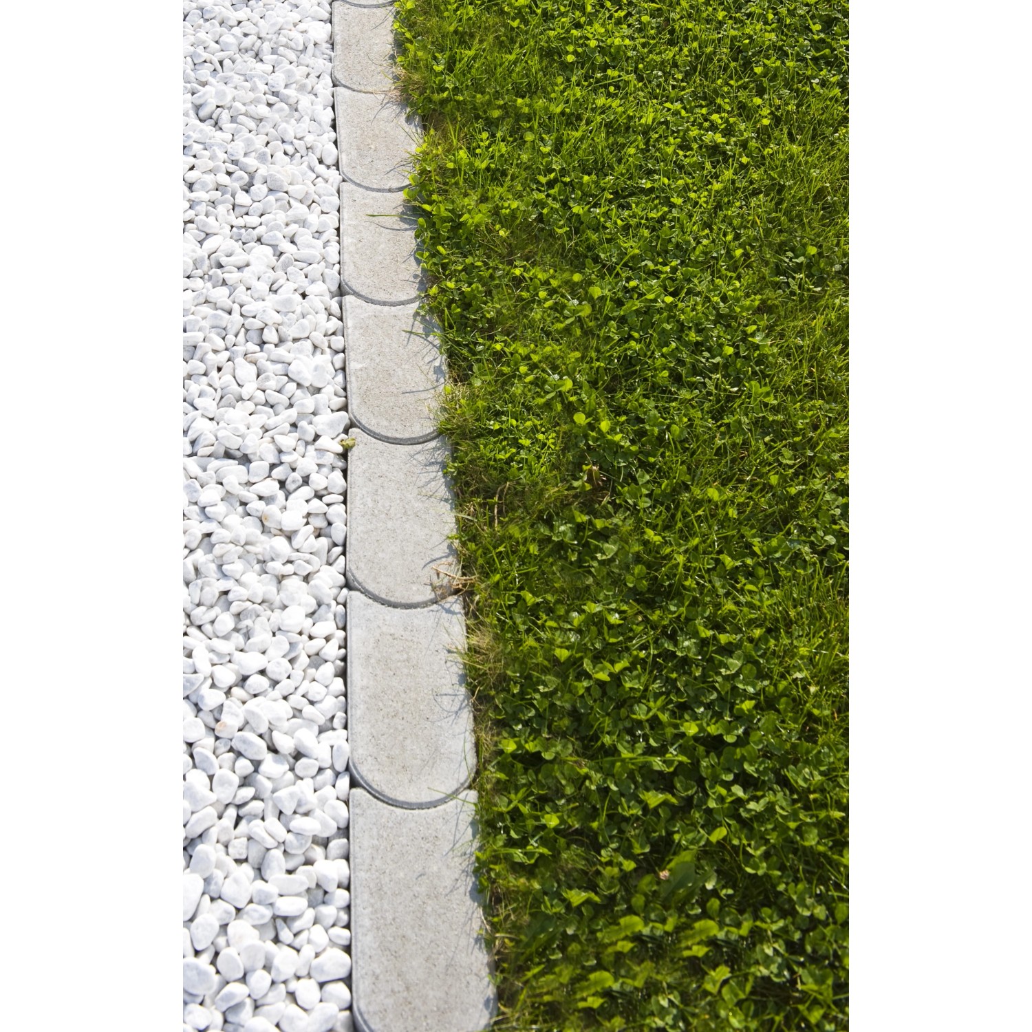 Graue Mähkante aus Beton zwischen Rasen und weißen Ziersteinen zur Gartengestaltung.