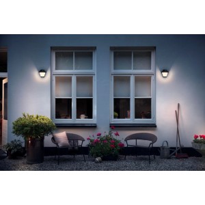 Schwarze Philips MyGarden Serres Außenwandleuchte an einer Hauswand mit Gartenmöbeln.