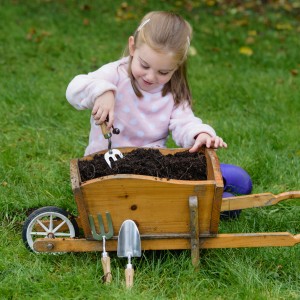 Mädchen hantiert mit Kent & Stowe Kinder-Handgabel in Schubkarre mit Erde. Gartenspaß für Kinder.