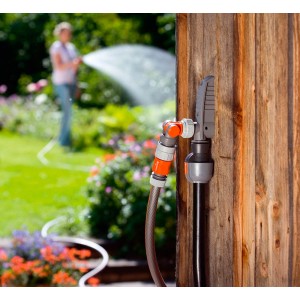 Gardena Wasserstecker an Holzwand mit angeschlossenem Gartenschlauch im Einsatz.