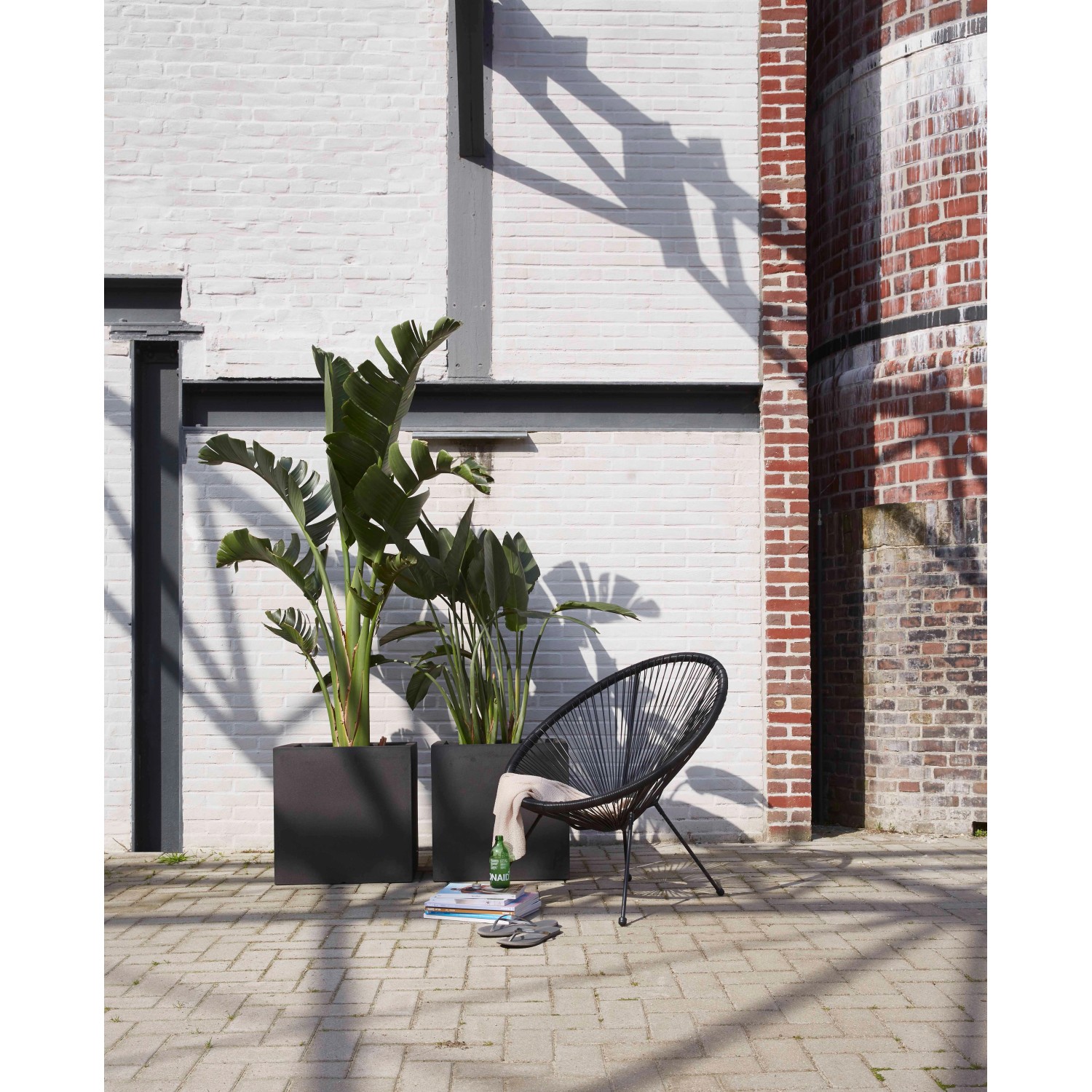 Schwarzer, viereckiger Capi Pflanztopf Smooth (50x50x50 cm) mit Pflanzen und Stuhl im Außenbereich.