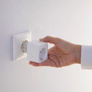 Hand steckt weißen WiZ Smart-Plug in Steckdose. Smart Home Steuerung für Lampen.