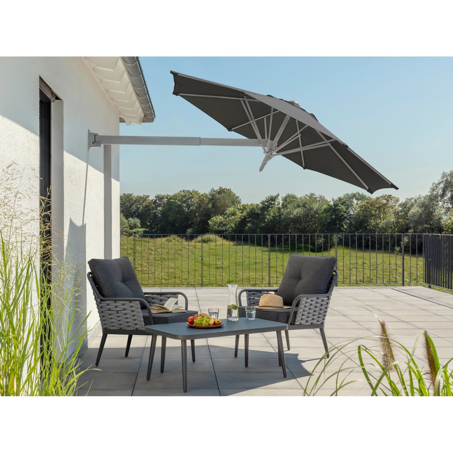 Anthrazitfarbener Schneider Ampelschirm Muro Ø 250 cm mit Handöffner über einer Sitzgruppe.