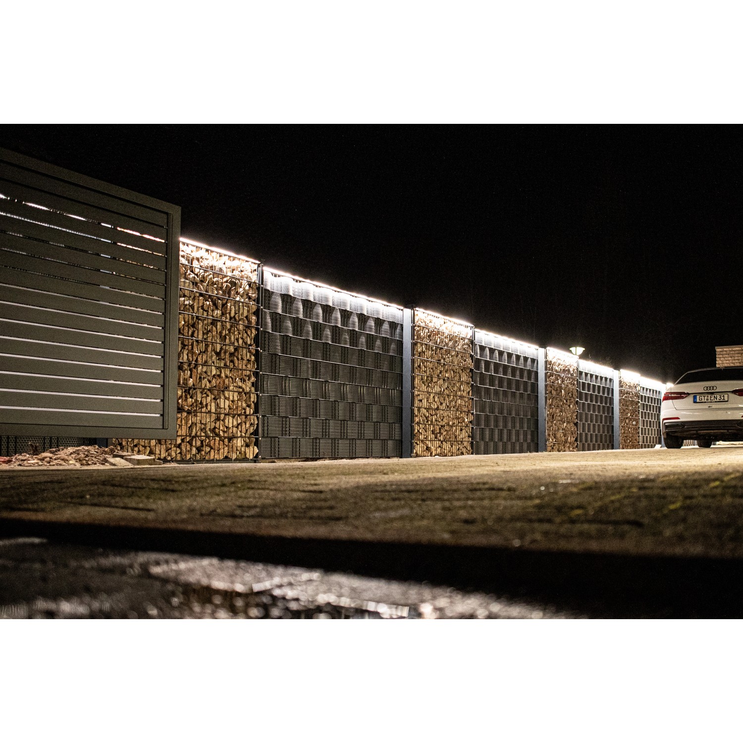 LyghtUp LED-Zaunbeleuchtung Set, anthrazit, beleuchtet einen Zaun mit Gabionen und einem Tor.