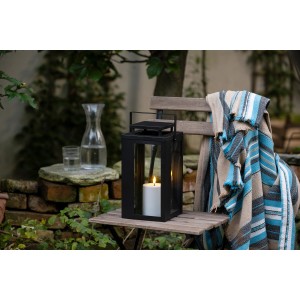Schwarze FlowerPower LED-Laterne Lucido Outdoor, 31 cm, mit Kerze auf einem Gartentisch.