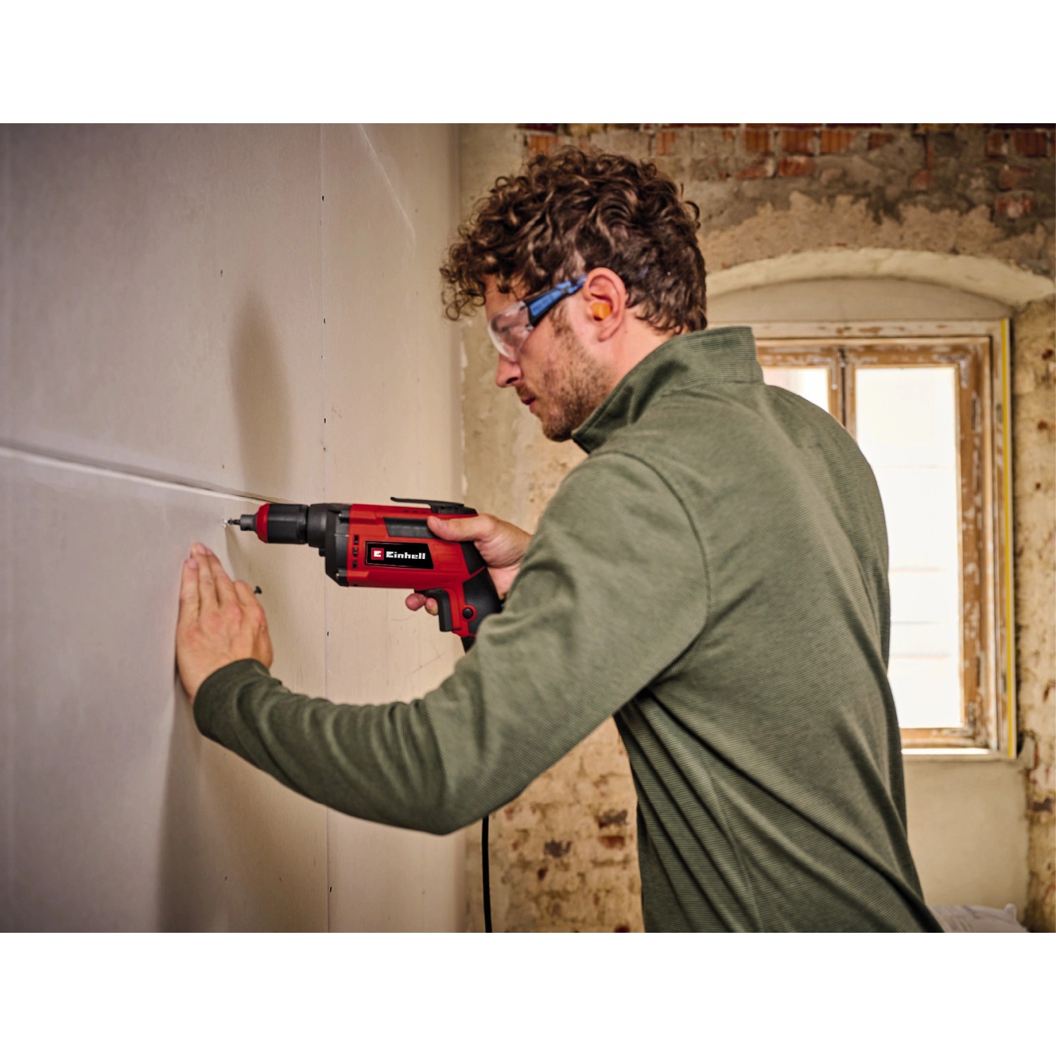 Einhell TC-DY 710 E Trockenbauschrauber in Nutzung, rot/schwarz, mit Mann und Schutzbrille.