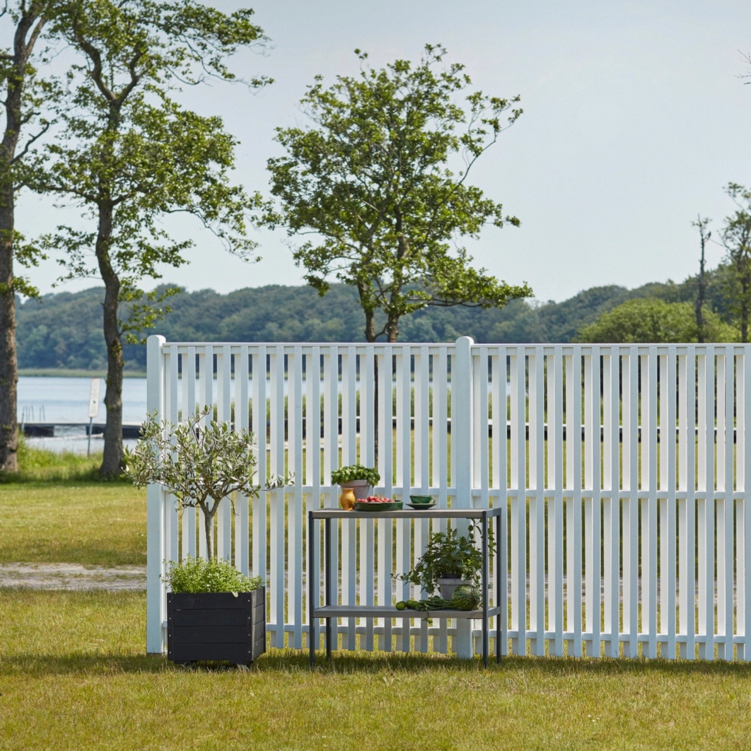Weißer Sichtschutzzaun Nagano aus Nadelholz, 180x140 cm, im Garten mit Pflanzen dekoriert.