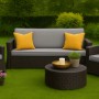 Graues Gartensofa mit Kissen und Rattansessel im Garten. Gemütliche Sitzgruppe für Terrasse und Balkon.