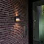 Moderne Lutec LED-Außenwandleuchte Lotus in Anthrazit mit Up & Down Lichteffekt an einer Backsteinwand.