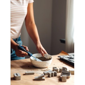 DIY Betonbuchstaben & -zahlen gießen: Frau mischt Beton in Schale, fertige Buchstaben liegen auf Tisch.