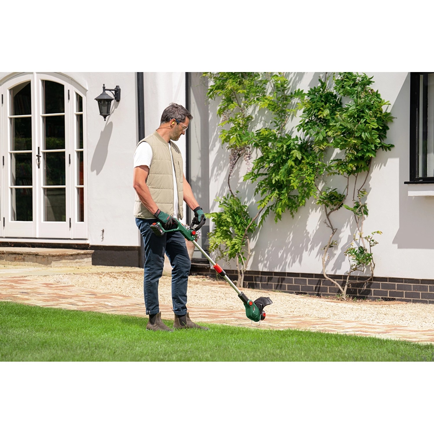 Mann trimmt Rasen mit Bosch Akku-Rasentrimmer UniversalGrassCut 18V-26-500.