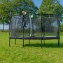 Rechteckiges, grünes Gartentrampolin mit Sicherheitsnetz und Person beim Klettern.