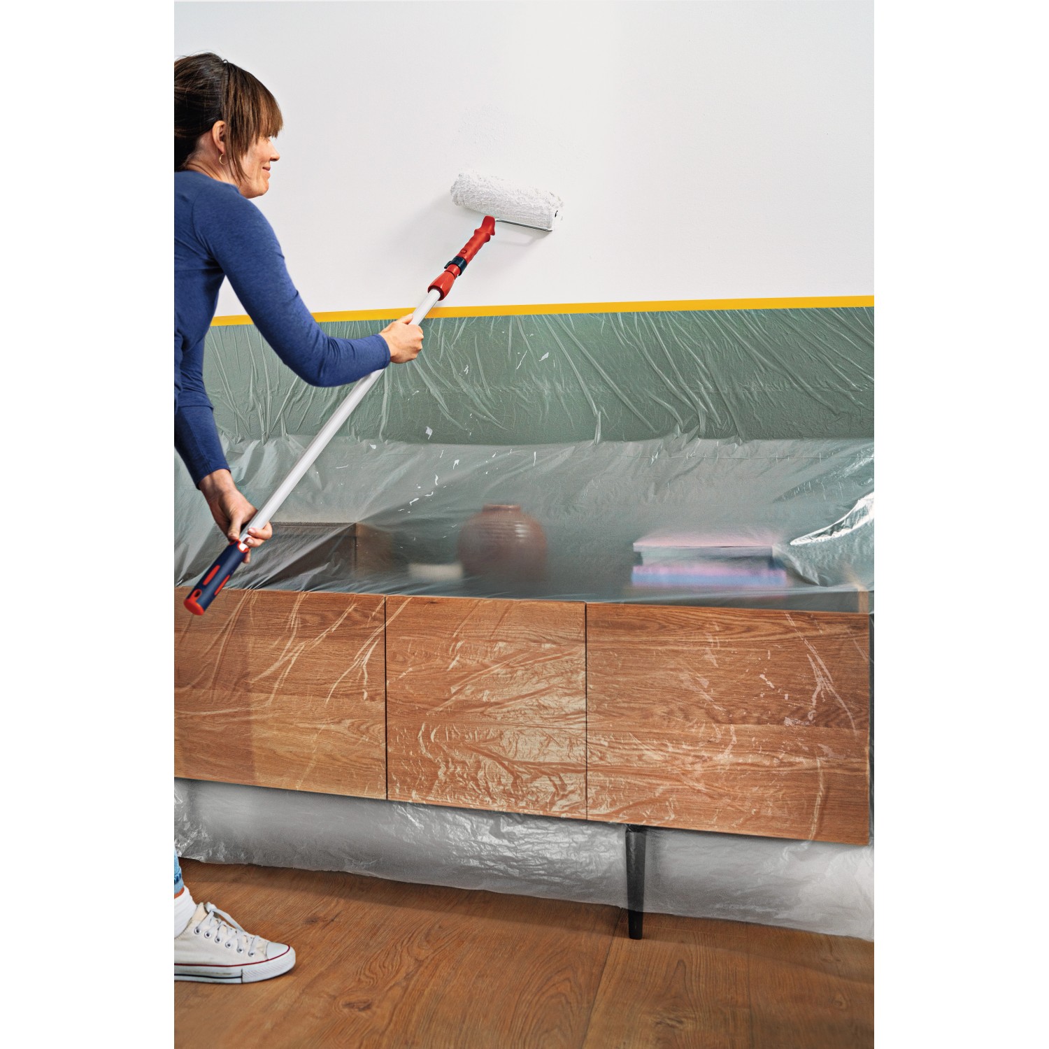 Frau streicht Wand mit Tesa Abdeckfolie Easy Cover Perfect+ L, Möbel abgedeckt.
