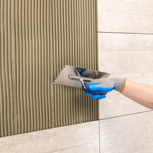 Auftragen von Knauf Flexkleber Naturstein mit Zahnspachtel auf Fliesen.