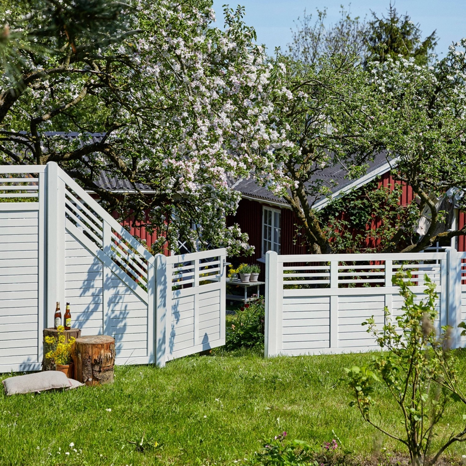 Weißer Sichtschutzzaun Decora aus Nadelholz, 180x180 cm, im Garten mit blühendem Baum.