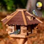 Sechseckiges Dobar Vogelhaus Blockhaus aus Holz mit rotem Bitumendach. Zwei Vögel fressen am Futterhaus.