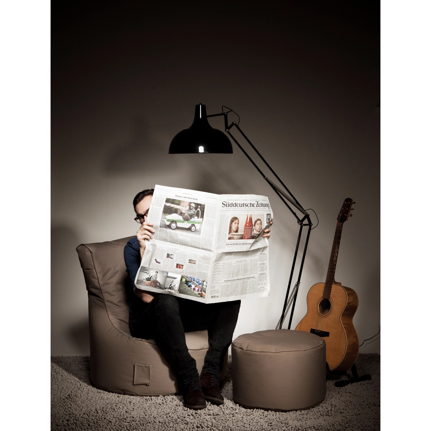 Sitting Point Sessel Swing Anthrazit mit Hocker, Mann liest Zeitung unter Lampe.