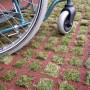 Rote Rasengitter-Fallschutzplatte 100x100 cm mit Rollstuhl befahrbar. Terrassenplatte mit Rasen.