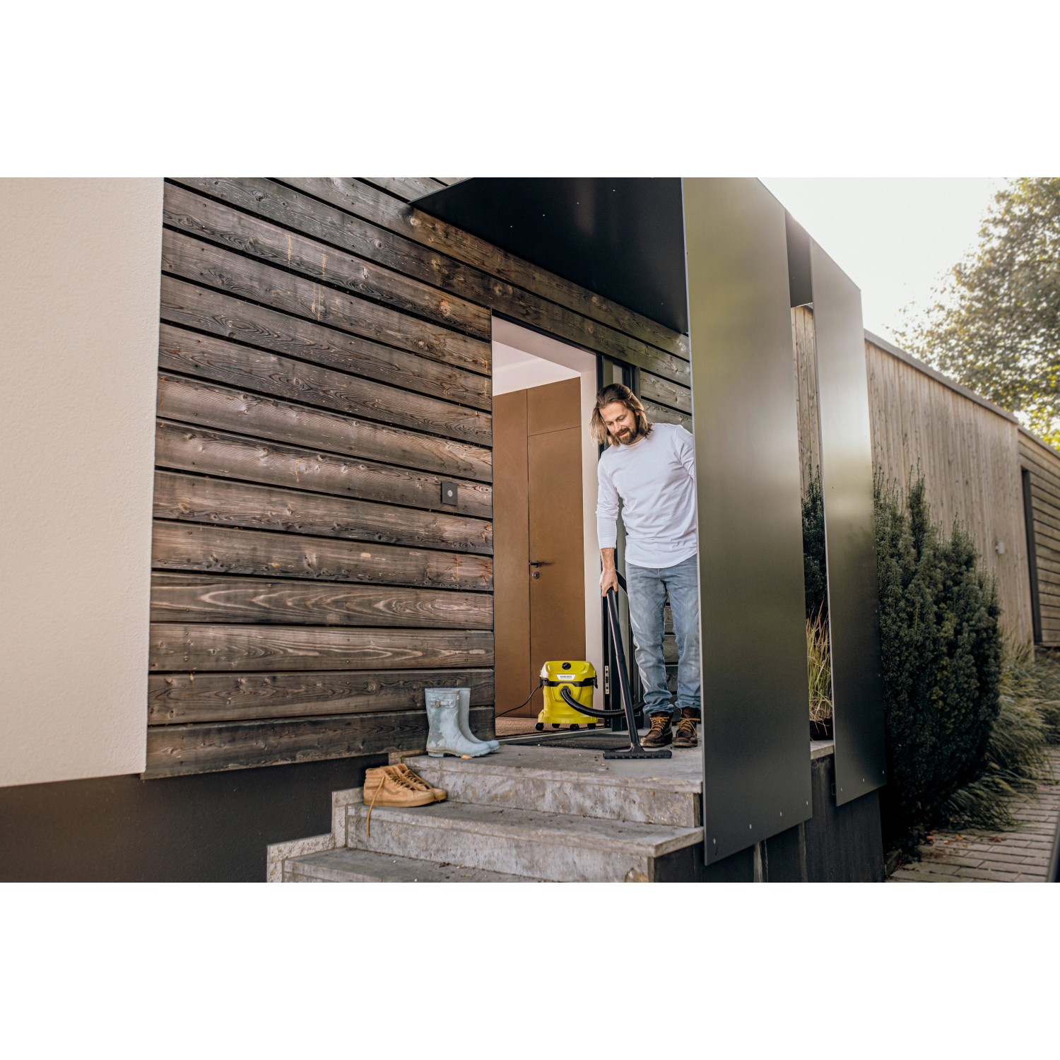 Mann saugt mit gelbem Kärcher WD 2 Plus Nass-Trockensauger Treppe vor Haus. Zubehör inklusive.