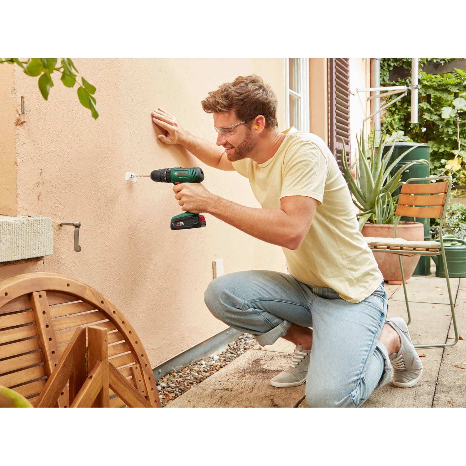 Mann bohrt mit Bosch Akku-Schlagbohrschrauber ein Loch in die Wand. Inkl. Akku und Koffer.