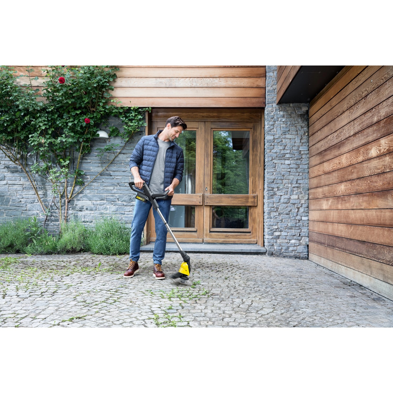 Mann nutzt Kärcher Akku-Unkrautentferner WRE 18-55 zur Unkrautentfernung auf Pflastersteinen.