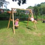 Axi Doppelschaukel aus Holz mit zwei Kindern im Garten.