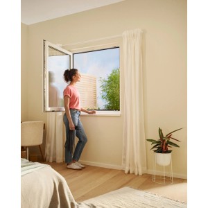 Frau am Fenster mit anthrazitfarbenem tesa® Insect Stop Fliegengitter Premium. Effektiver Insektenschutz.