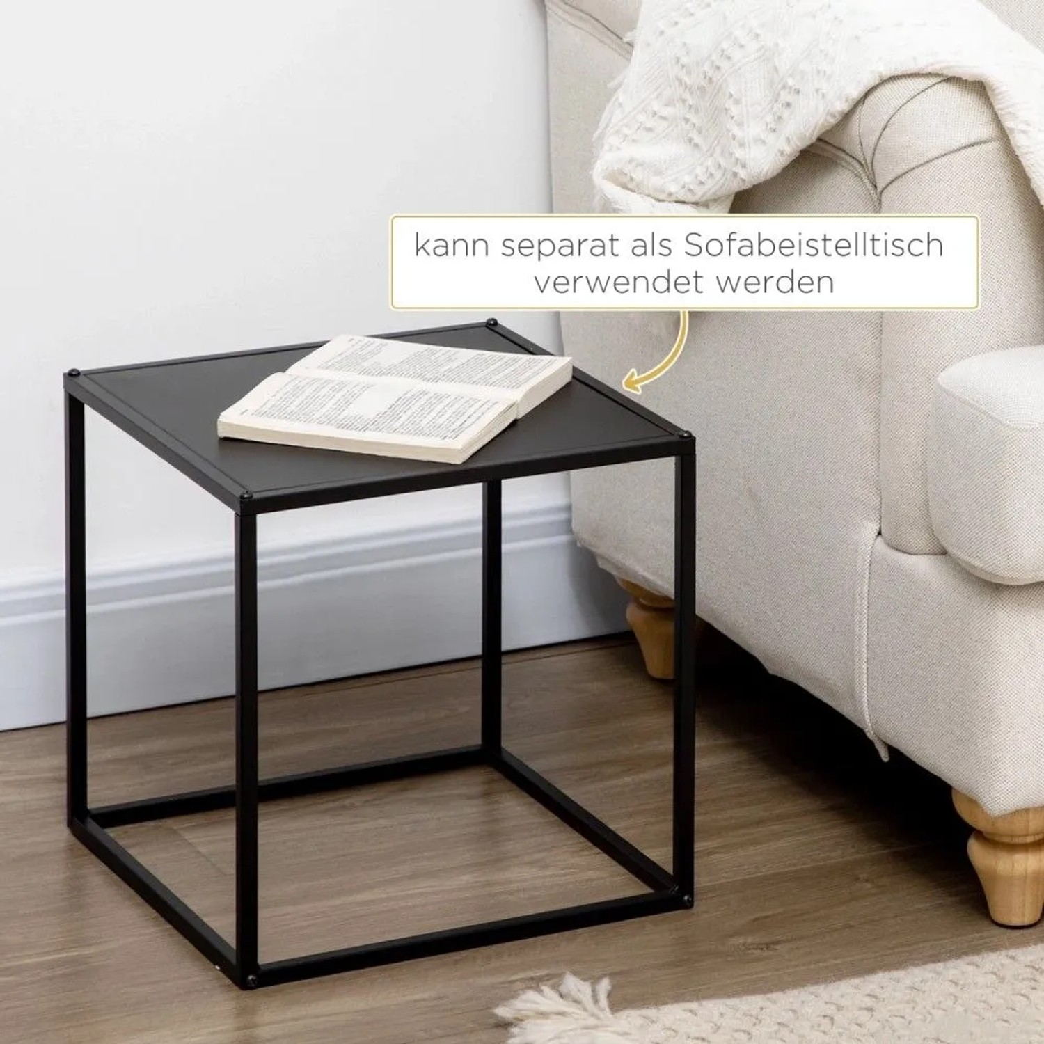 Schwarzer, eckiger Couchtisch aus Stahlgestell neben einem Sofa, mit Buch. Ideal als Beistelltisch im Wohnzimmer.