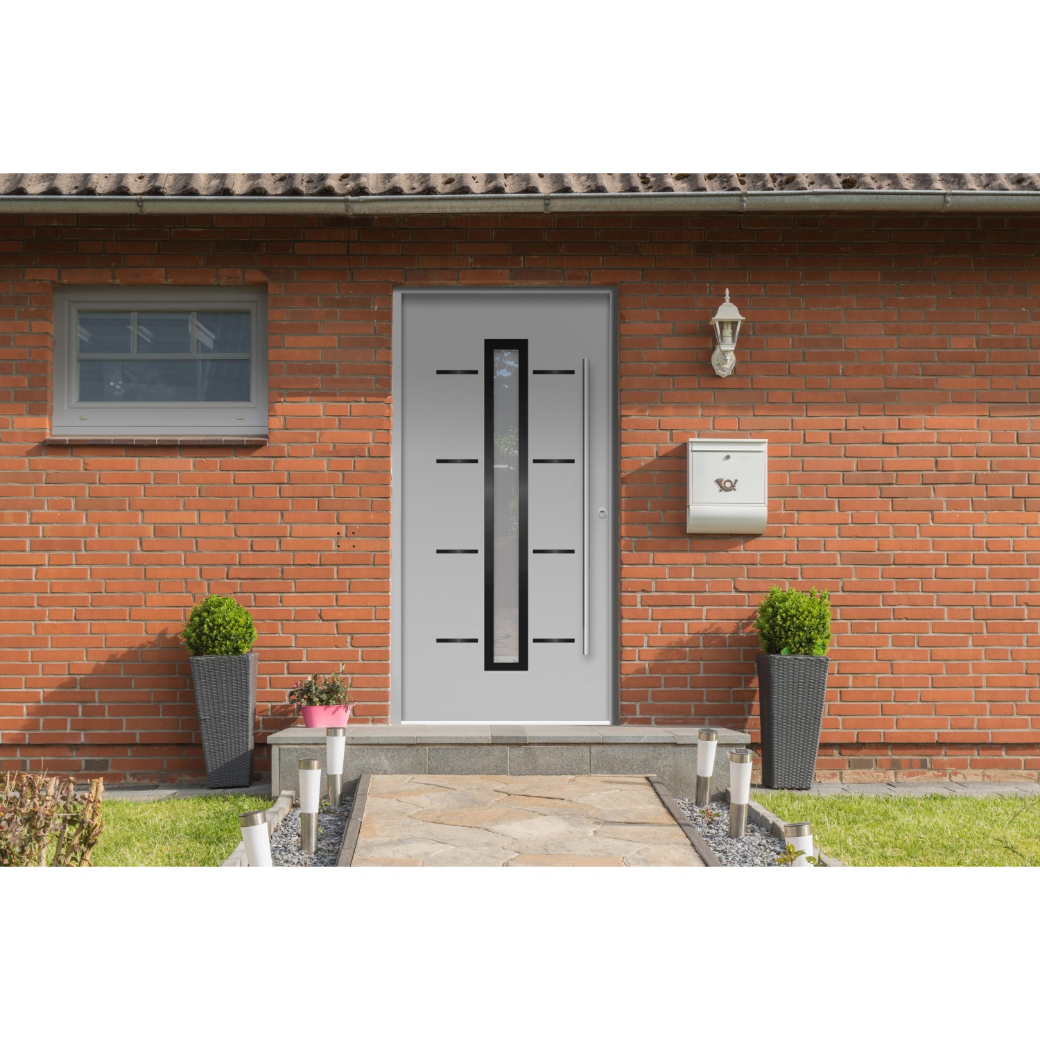 Graue Sicherheits-Haustür ThermoSpace Milano RC2 mit Glaseinsatz und Edelstahlgriff vor Backsteinhaus.