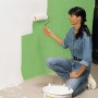 Frau streicht Wand mit Farbroller, LUX Auslegepapier zum Abdecken empfohlen.