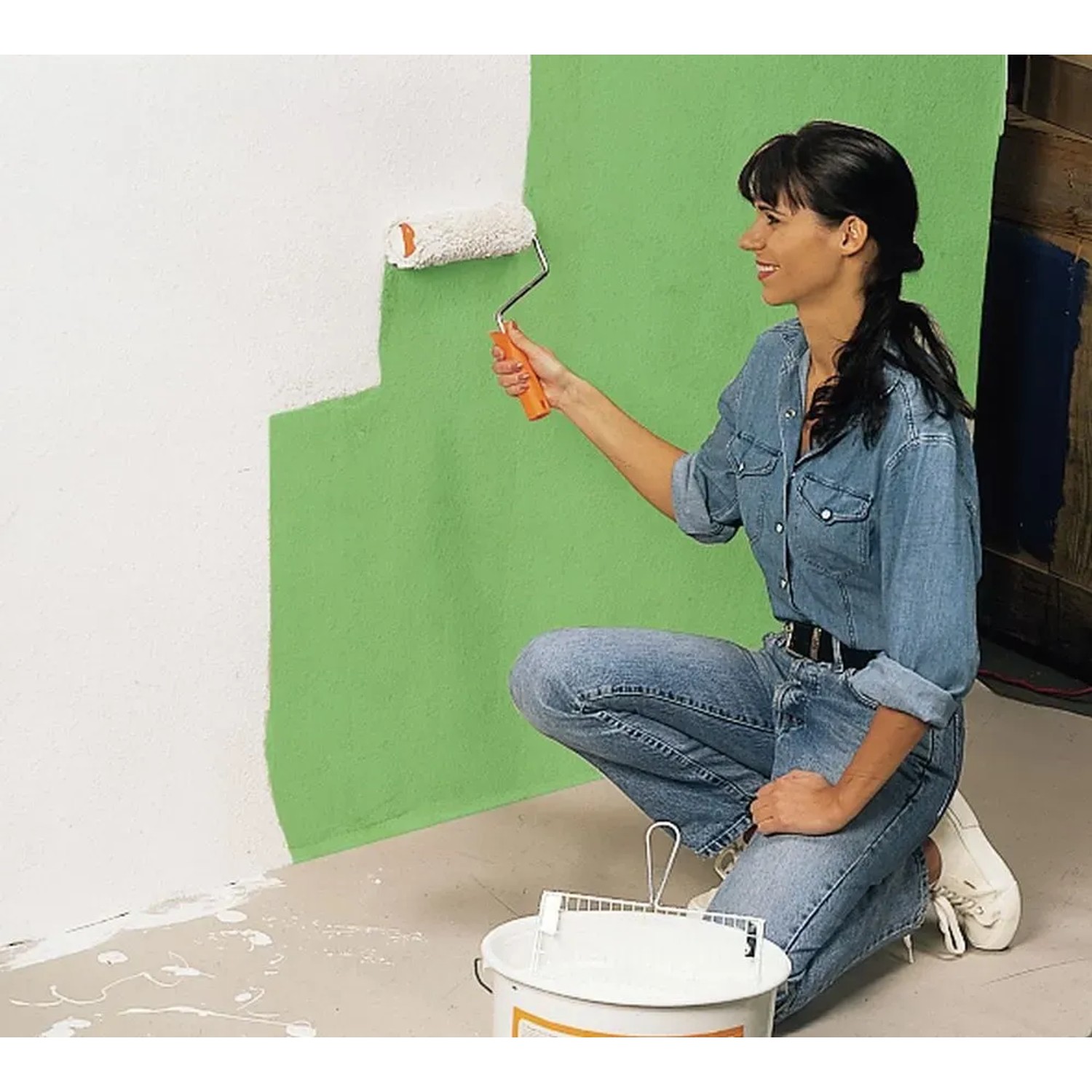 Frau streicht Wand mit Farbroller, LUX Auslegepapier zum Abdecken empfohlen.