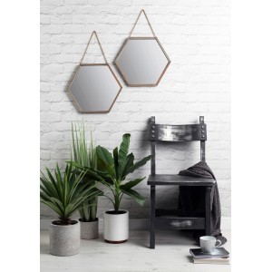 Zwei sechseckige Spiegel mit silbernem Rahmen an einer weißen Ziegelwand, kombiniert mit Pflanzen und einem Stuhl.