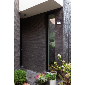 Schwarze Lutec LED Solar-Wandleuchte Tuda mit Bewegungsmelder an dunkler Hauswand.