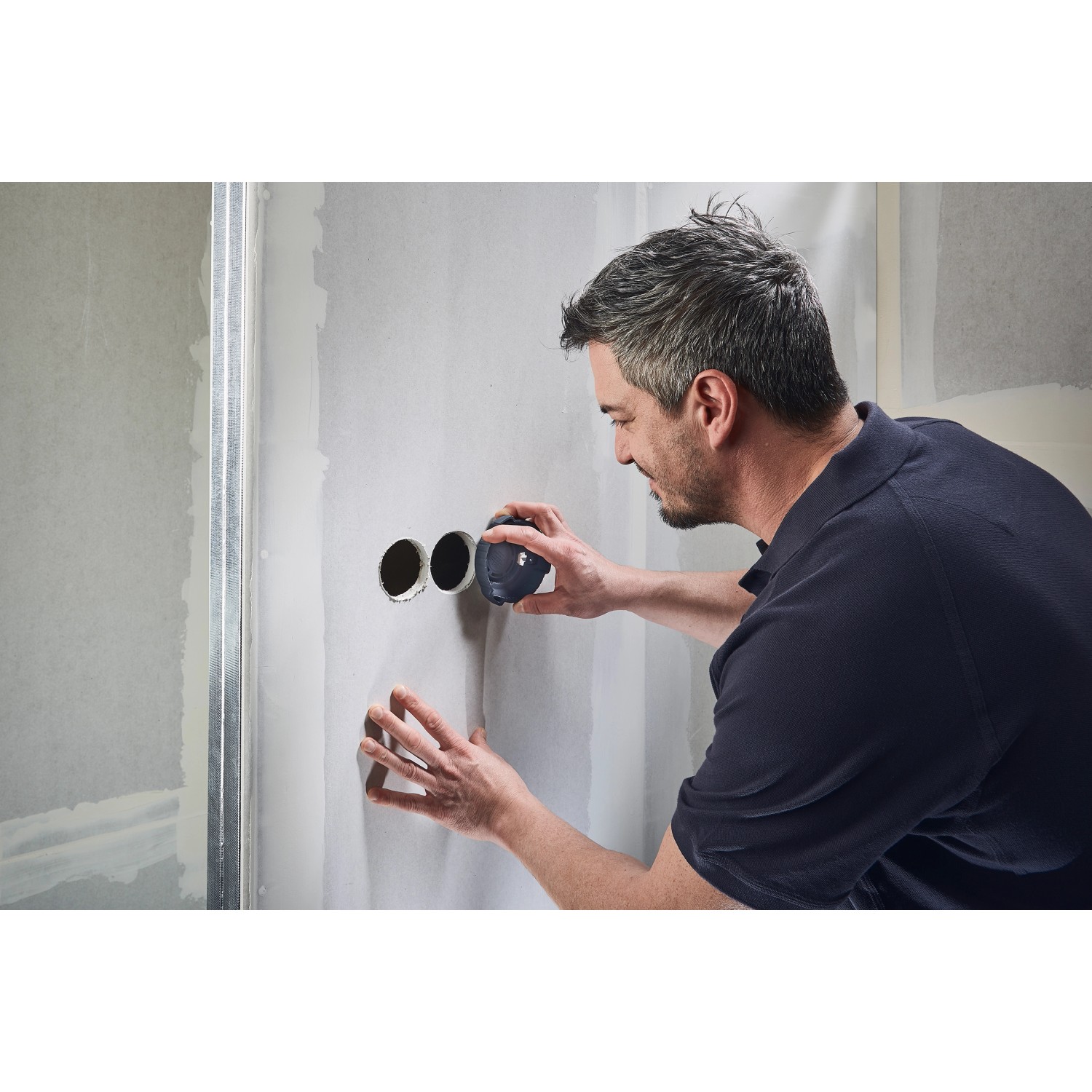 Mann senkt Lochränder mit wolfcraft Lochrandsenker (Ø 68 mm) in Gipskartonwand. Lochsäge für Hohlwanddosen.