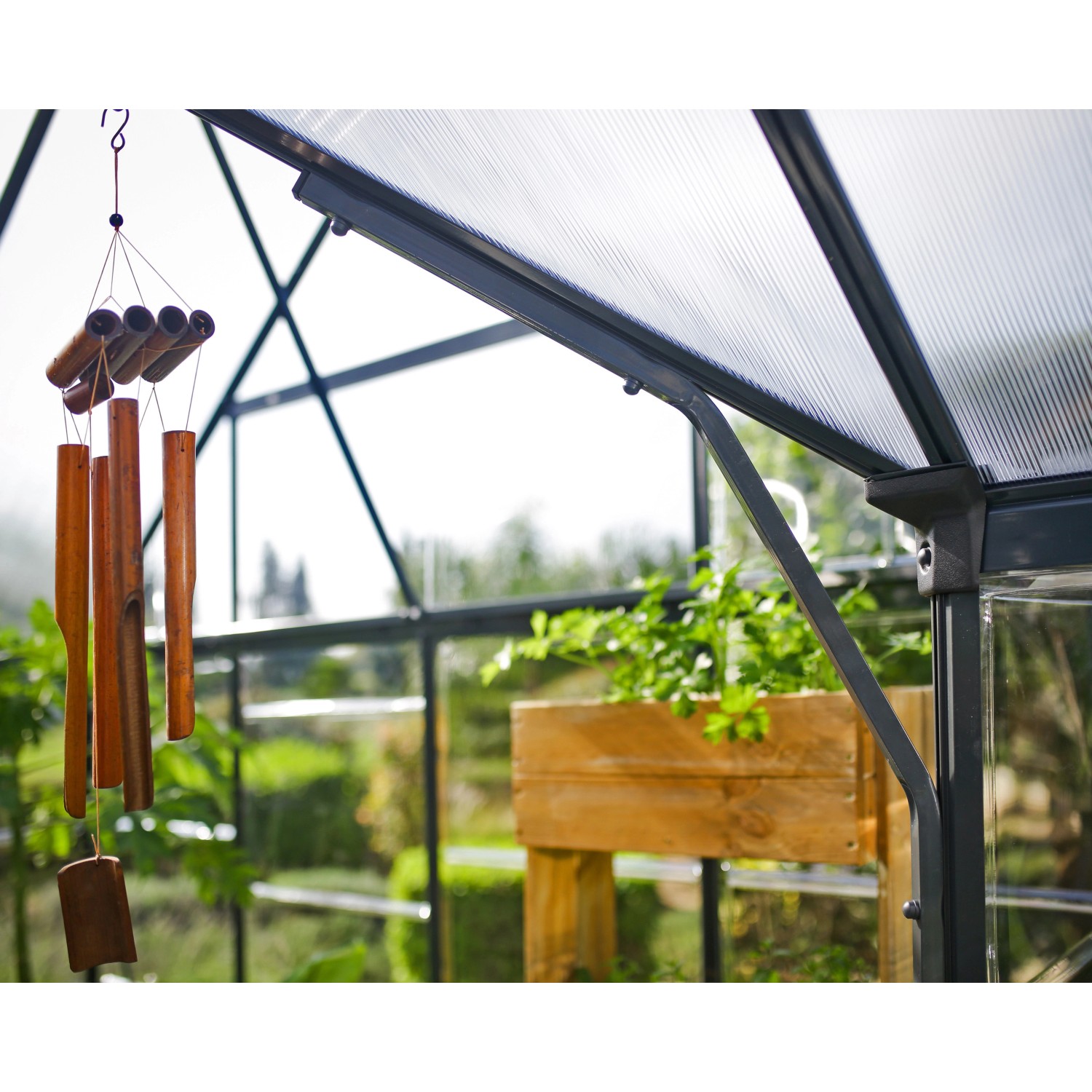 Detailaufnahme: Palram Canopia Victory Orangerie Gewächshaus mit Pflanzen und Windspiel.