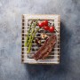 Einweg Casus Grill mit Steak, Tomaten und Gemüse auf dem Grillrost.